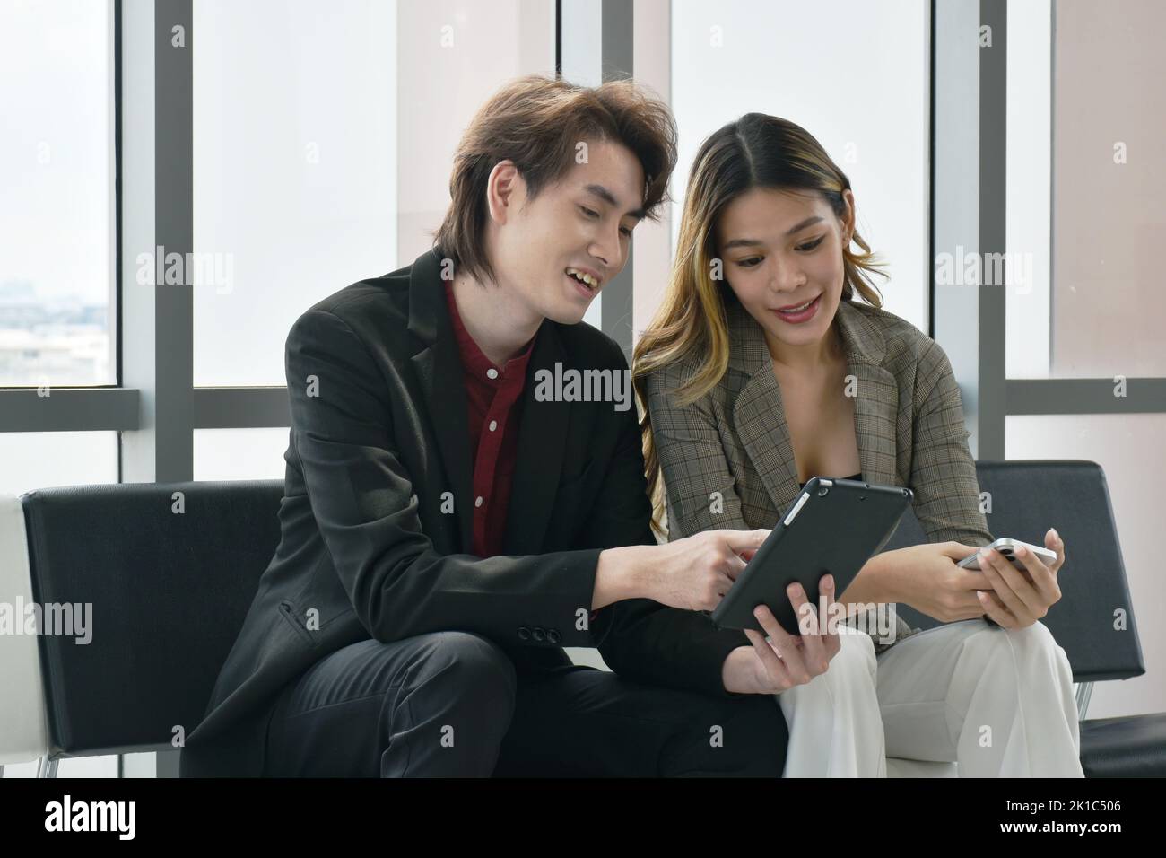 Felice uomo e donna asiatico busimess guardando il telefono cellulare per rilassarsi dopo il lavoro in ufficio Foto Stock
