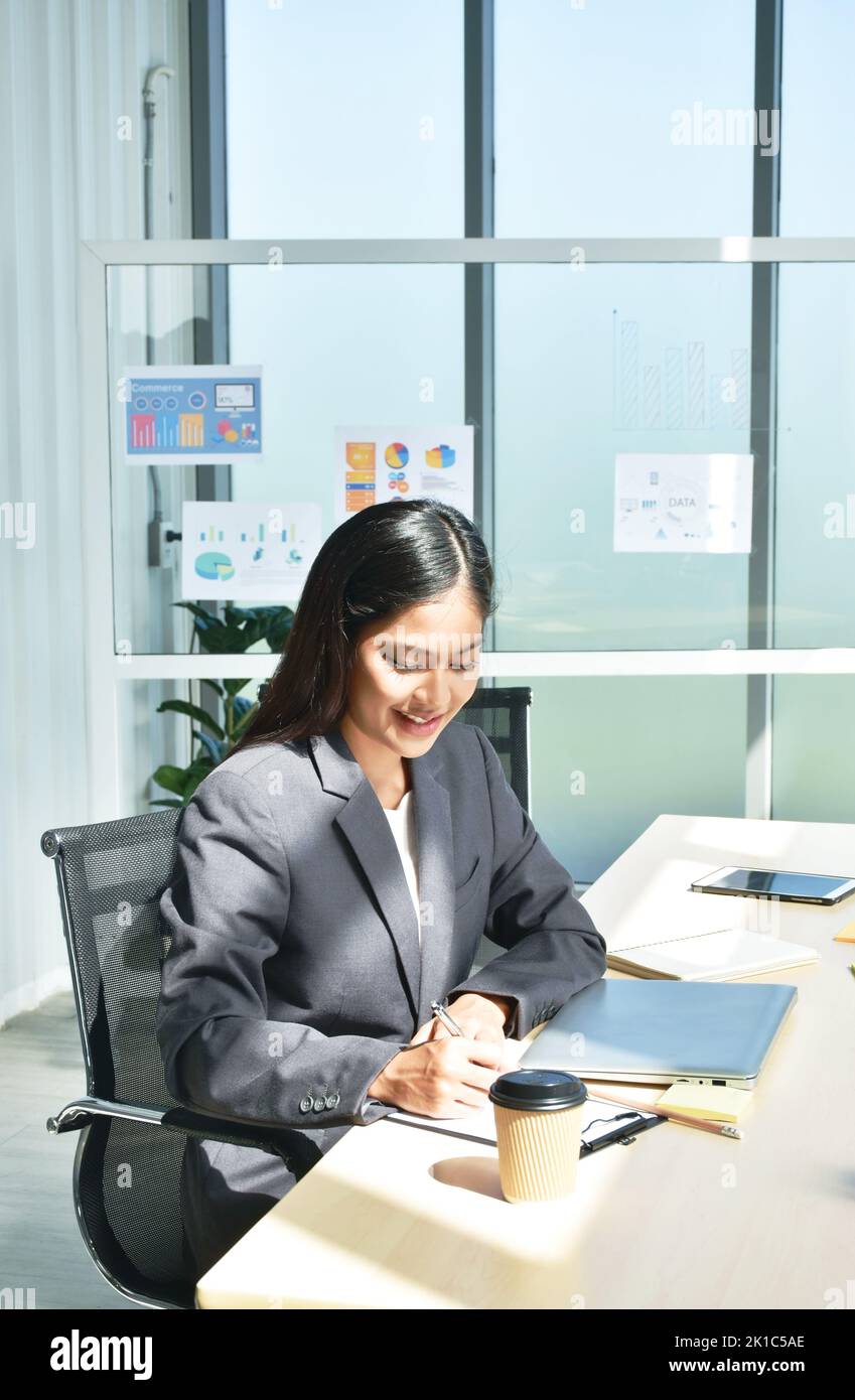 Felice donna asiatica d'affari nota sul libro e sul lavoro in ufficio Foto Stock