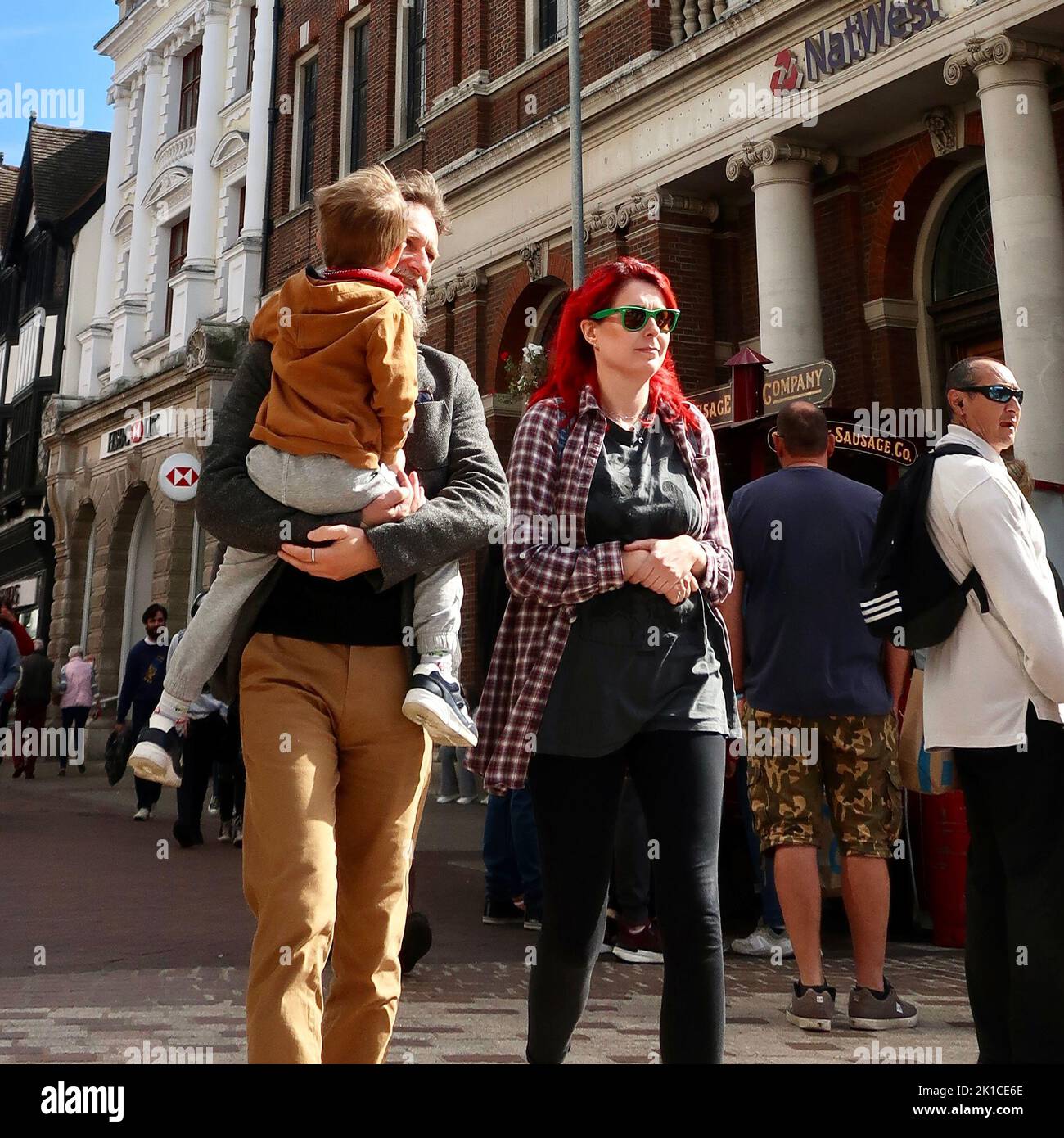 Ipswich, Suffolk, UK - 17 settembre 2022 : Una famiglia di tre persone a piedi attraverso il centro della città. L'uomo porta con sé un bambino. La donna ha capelli rossi luminosi e occhiali da sole con cornice verde. Foto Stock