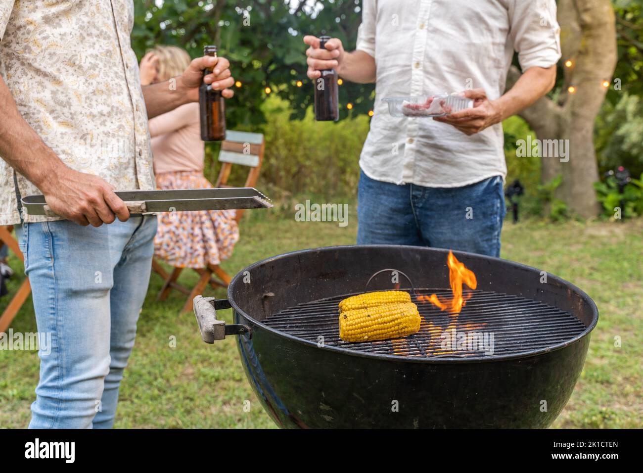 Cucinare con il barbecue di mais e carne. Fuoco e fumo sulla griglia e birra nelle mani. Foto Stock