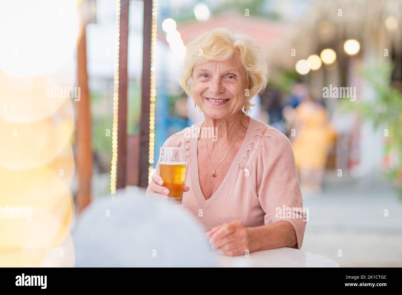 Donna matura seduta a un tavolo in un bar estivo e bere birra Foto Stock