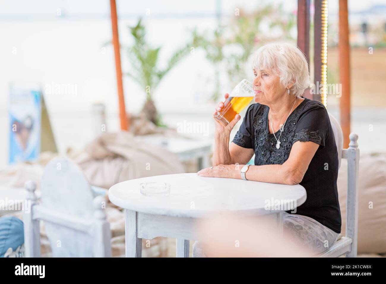 Donna matura seduta a un tavolo in un bar estivo e bere birra Foto Stock