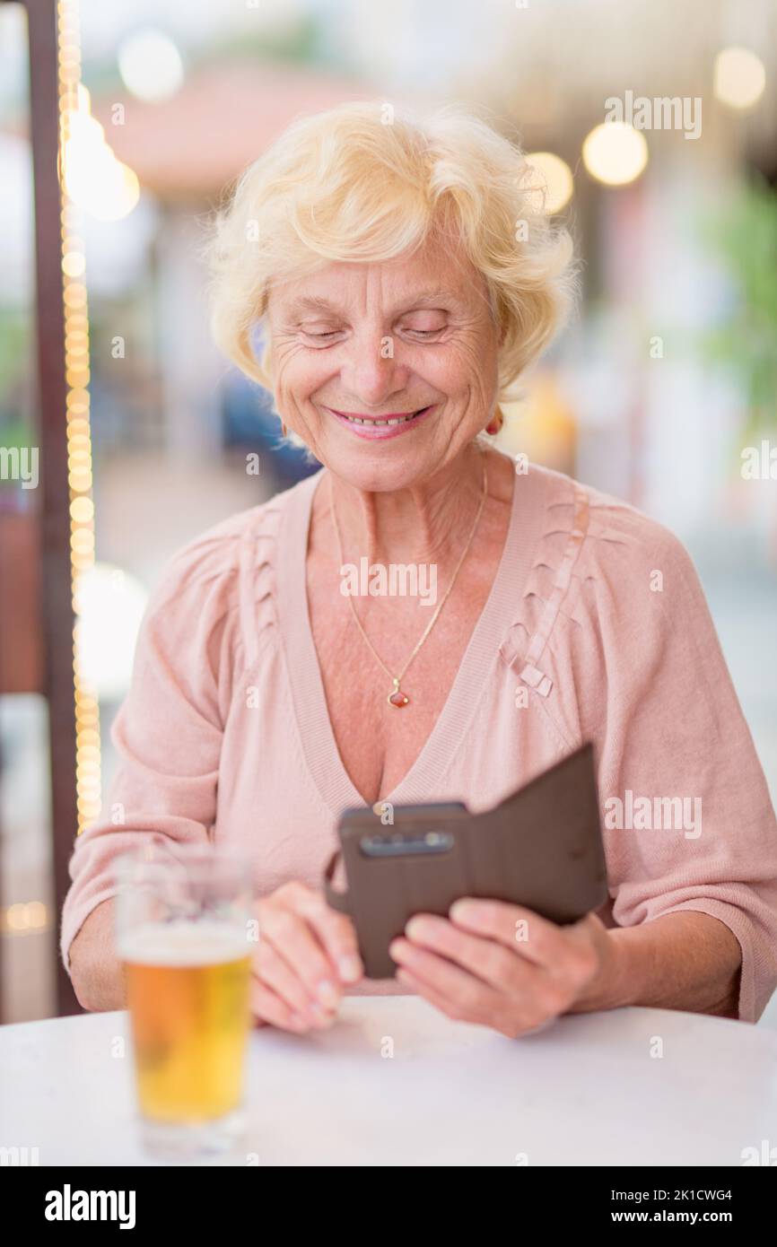 Donna matura seduta a un tavolo in un bar estivo e bere birra Foto Stock