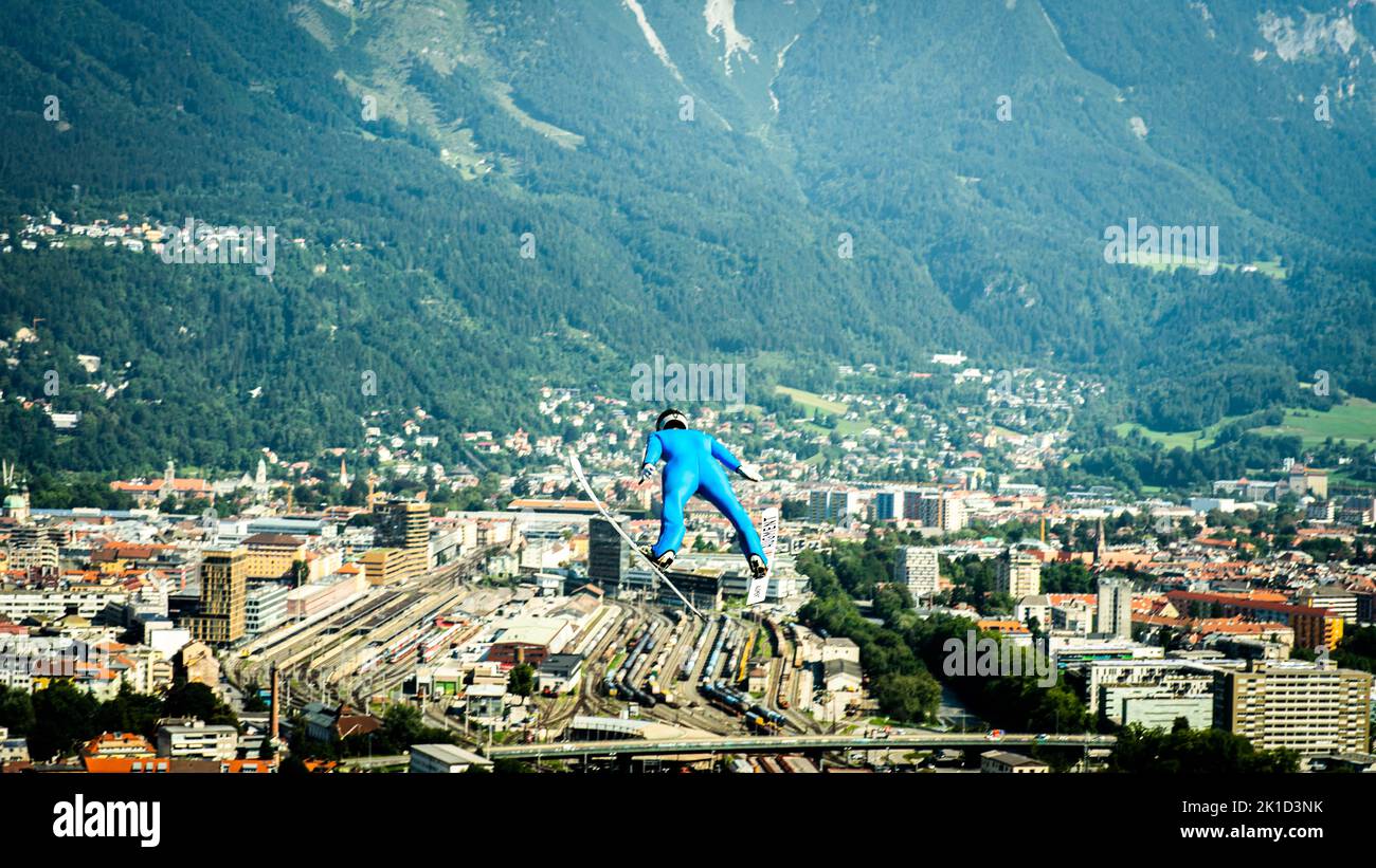 Uno sciatore in costume blu che salta contro un paesaggio urbano Foto Stock