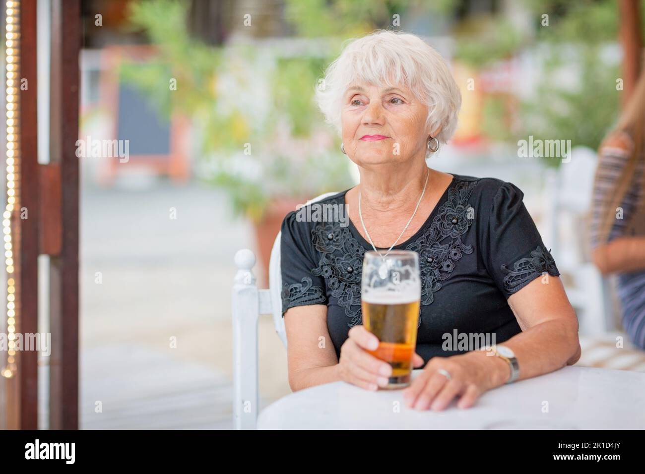Donna matura seduta a un tavolo in un bar estivo e bere birra Foto Stock