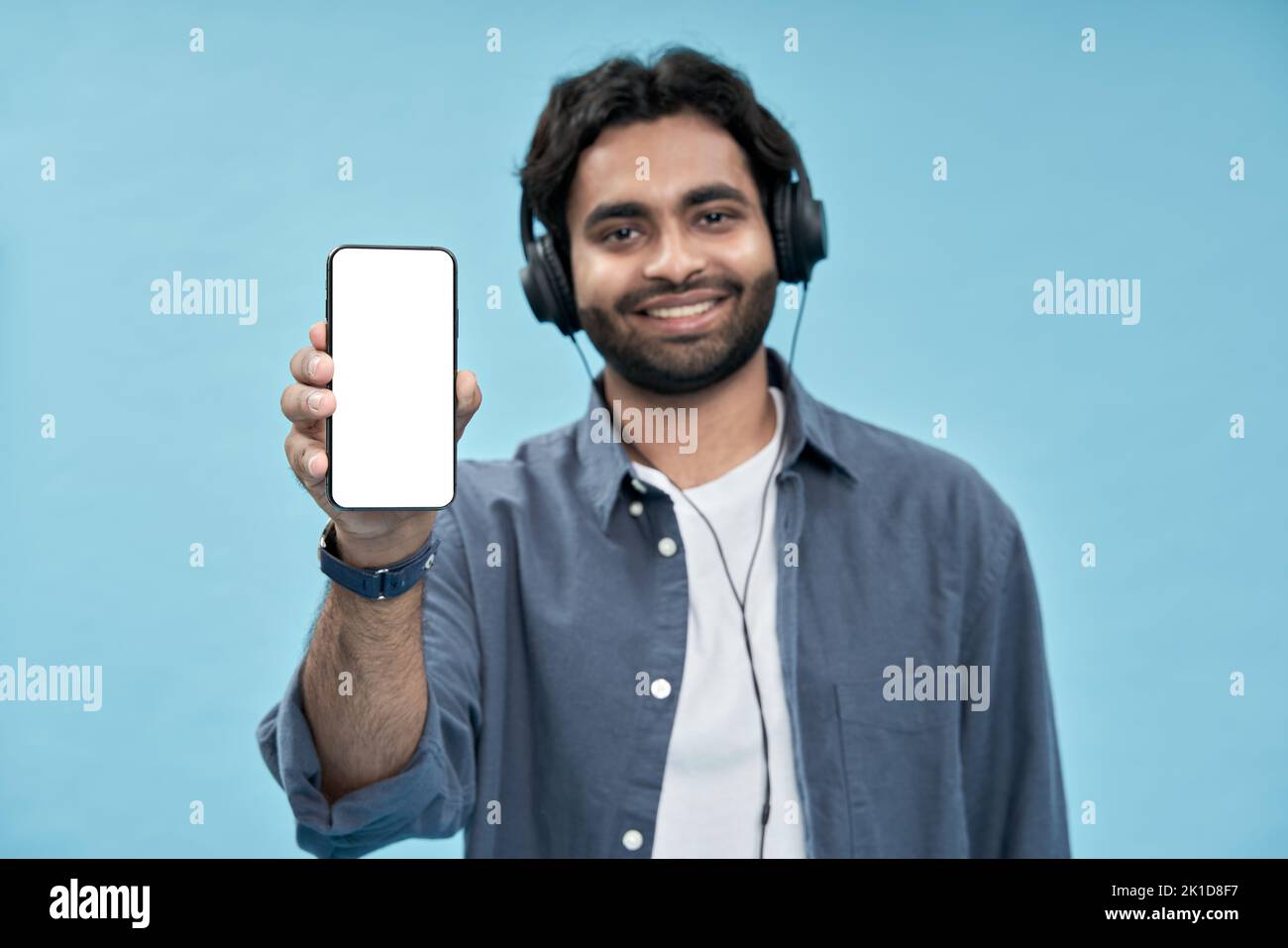 Felice uomo arabo che mostra il telefono cellulare mockup schermo isolato su blu. Foto Stock