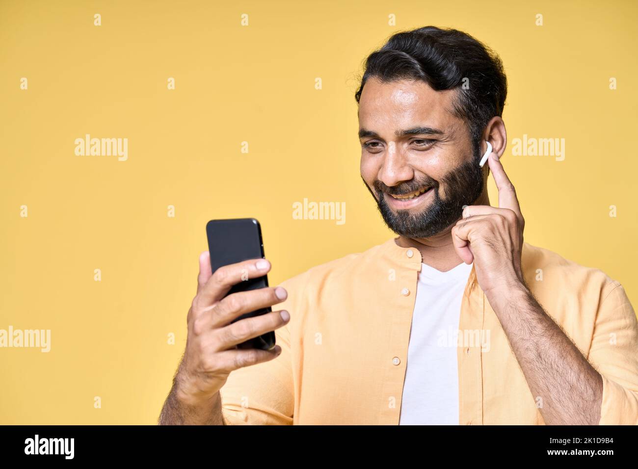 Felice uomo indiano che indossa gli auricolari utilizzando il telefono cellulare effettuare videochiamate. Foto Stock