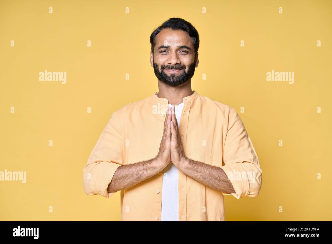 Uomo indiano felice memore meditando tenendo le mani in namaste isolato su giallo. Foto Stock