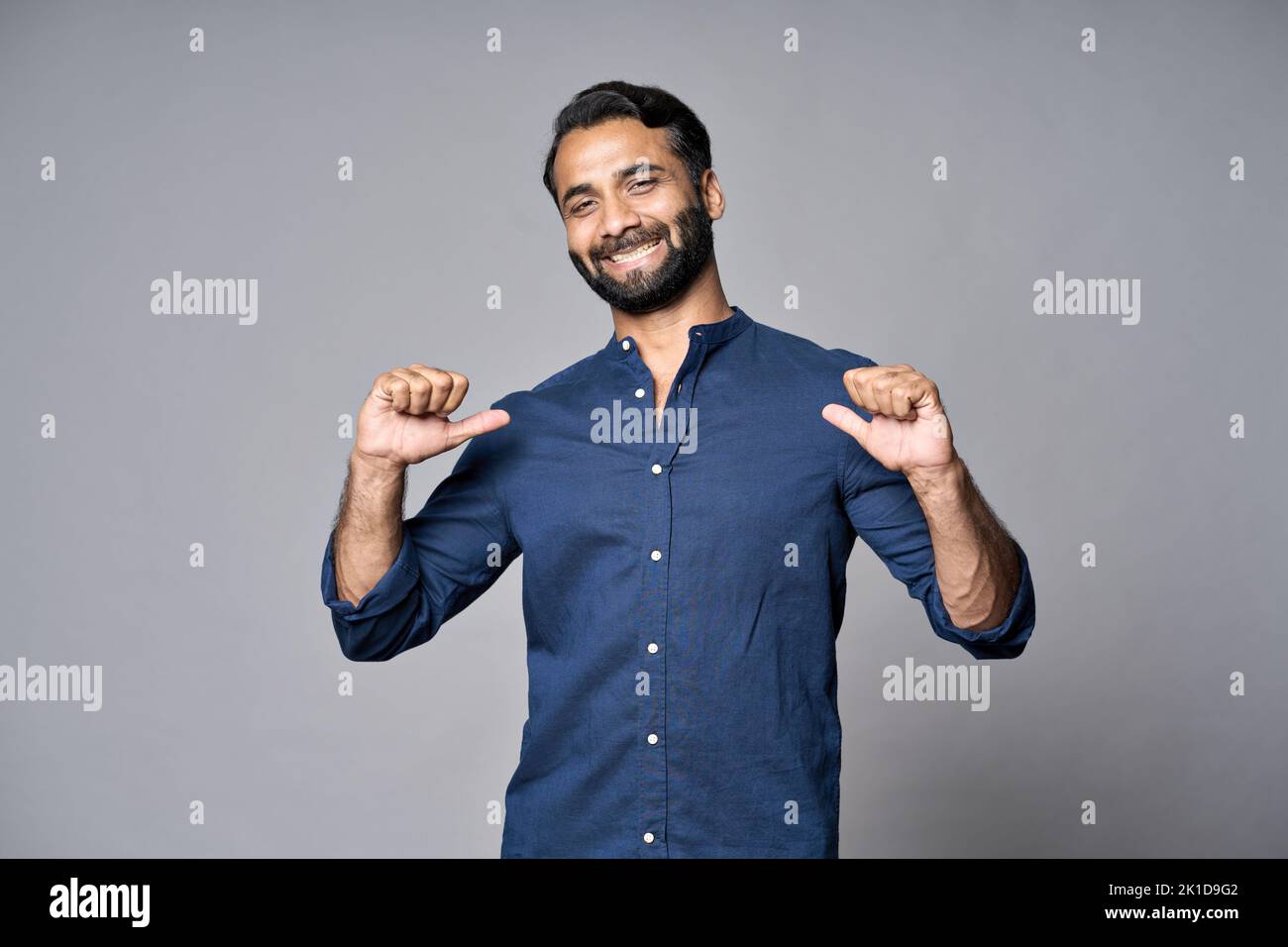 Uomo d'affari indiano sorridente in piedi isolato sul grigio che indica se stesso. Foto Stock