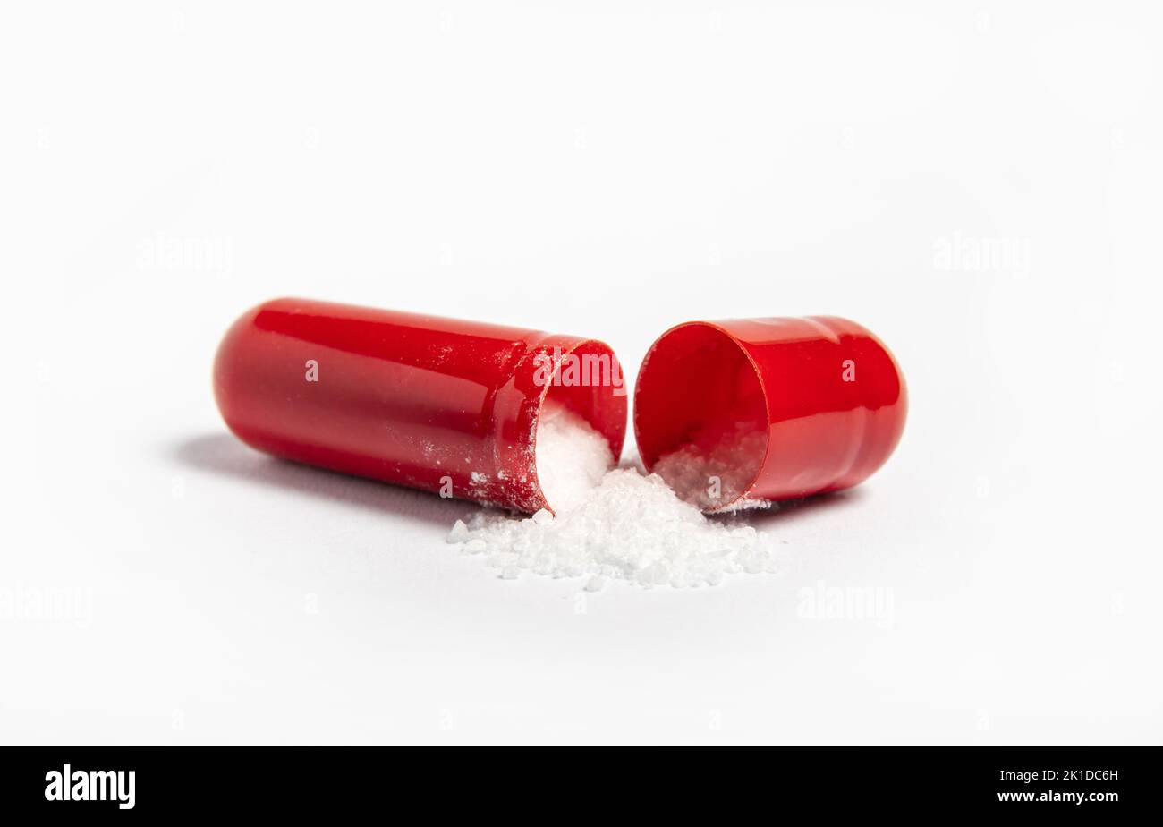 Vista laterale di una singola capsula di gel di colore rosso aperta, fuoriuscita di polvere di cristallo bianco, isolata su sfondo bianco. Concetto farmaceutico. Foto Stock