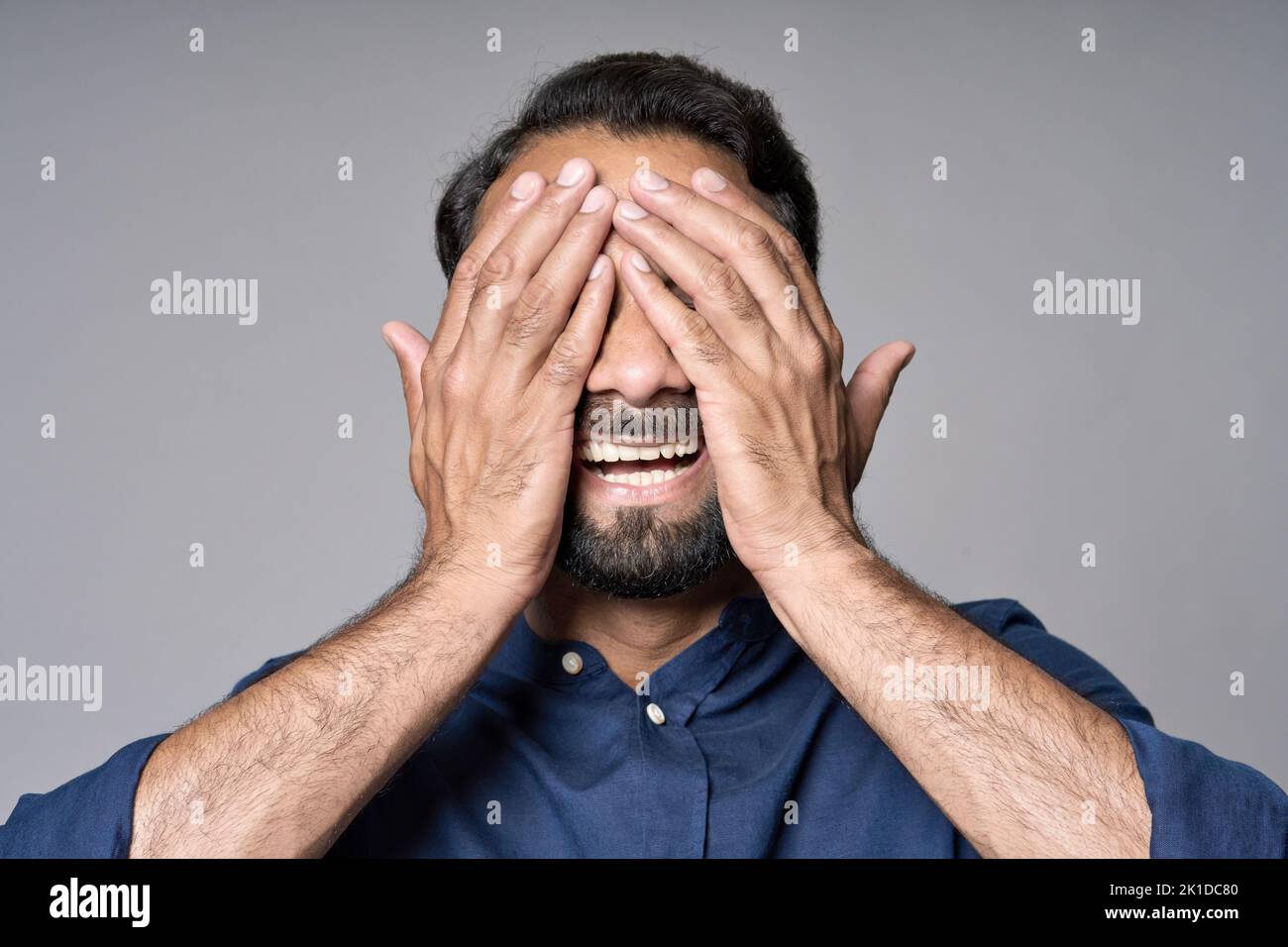 Uomo indiano felice che chiude gli occhi con le mani isolate su fondo grigio. Foto Stock