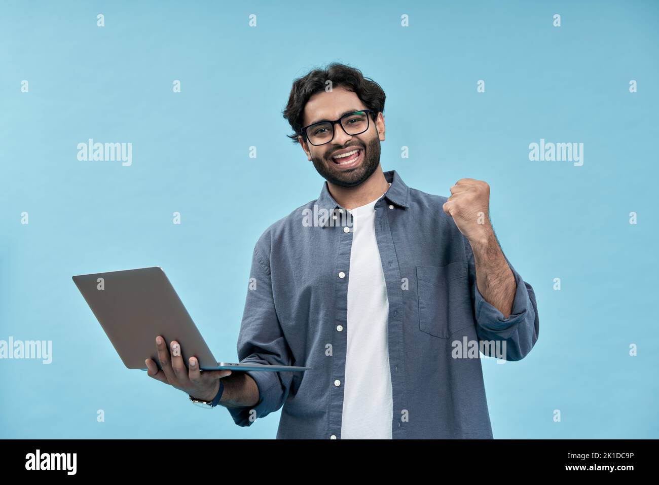 Felice giovane uomo arabo che celebra la vittoria tenendo isolato il portatile su blu. Foto Stock