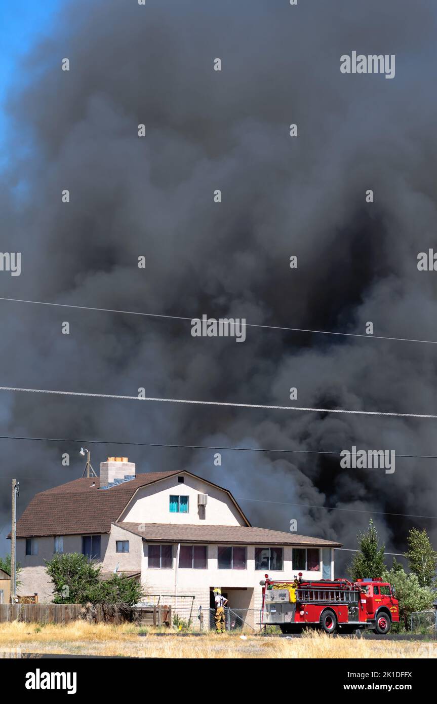 Pompiere e camion da fuoco davanti a un fuoco di casa con enormi nuvole di fumo incandescente. Foto Stock