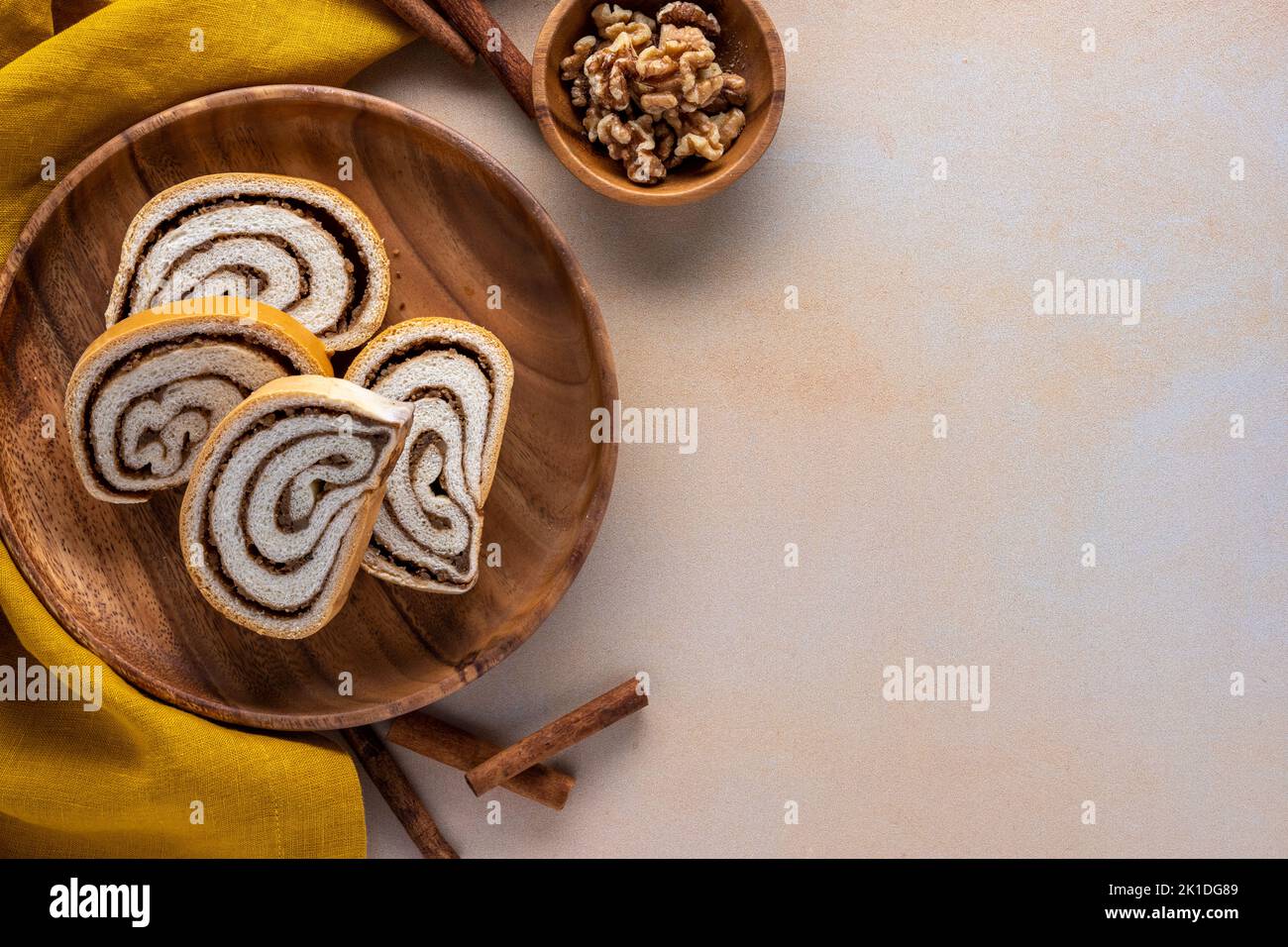 rotolo di noci su un piatto di legno con ciotola piccola di noci cannella bastoncini e tovagliolo su uno sfondo testurizzato Foto Stock