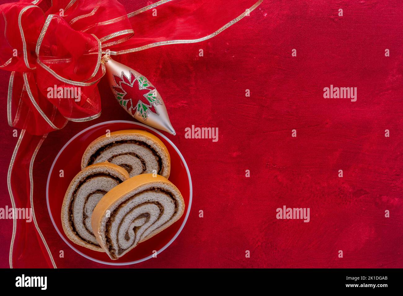 Piatto da dessert di Natale con rotolo di noci e sfondo rosso testurizzato, nastro e ornamento Foto Stock