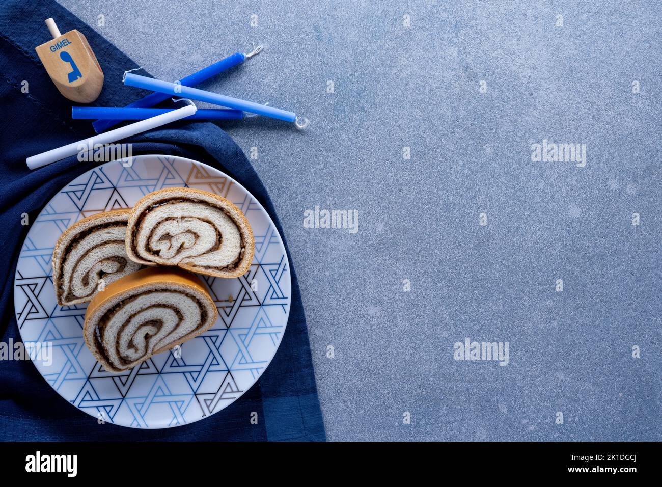 Piatto del deserto di Hanukkah con rotolo di noci, candele, dreidel e tovagliolo su sfondo blu strutturato Foto Stock