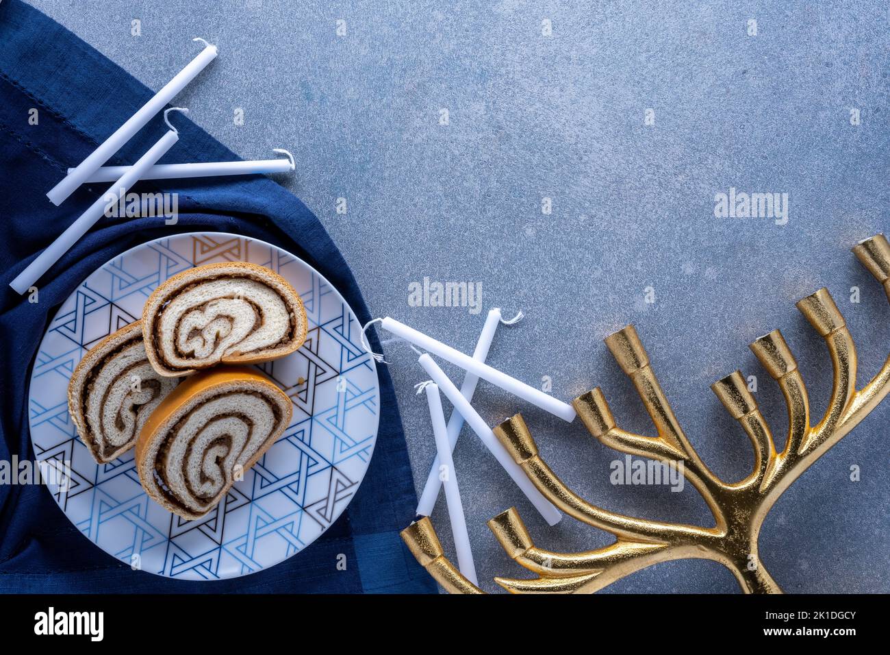 Piatto del deserto di Hanukkah con rotolo di noci, candele bianche e menorah dorata su sfondo blu strutturato Foto Stock