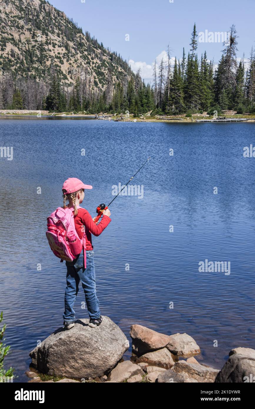 Ragazza con pigtail e cappello rosa pesca da una roccia a Notch Lake, Uinta Mountains, Mirror Lake Highway, Kamas, Utah, STATI UNITI Foto Stock