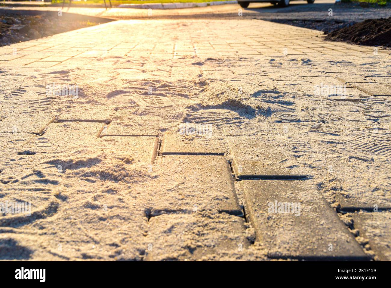 lastre di pavimentazione in pietra artificiale in fase di riempimento dei giunti con sabbia setacciata asciutta, messa a fuoco selettiva e retroilluminazione Foto Stock