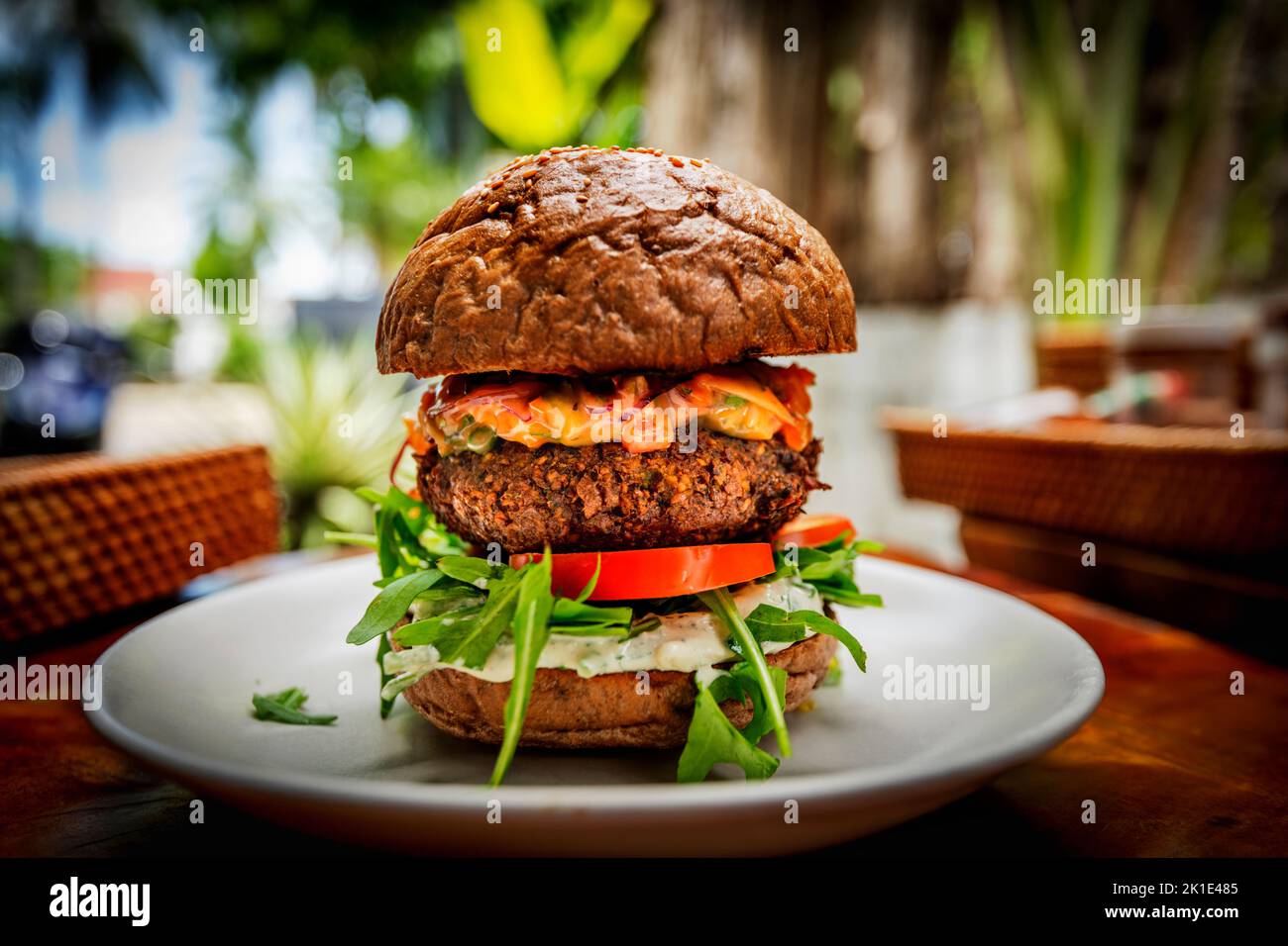 Hamburger vegano non di carne su un panino su un piatto bianco con pomodoro, salsa speciale, razzo. Foto Stock