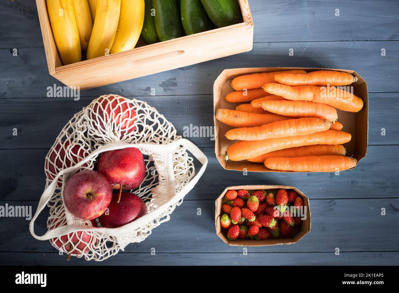 Verdure e frutta assortite in confezioni riutilizzabili di carta, legno e tessuto poste su un tavolo di legno blu. Concetto di imballaggio ecocompatibile. Vista dall'alto. Foto Stock