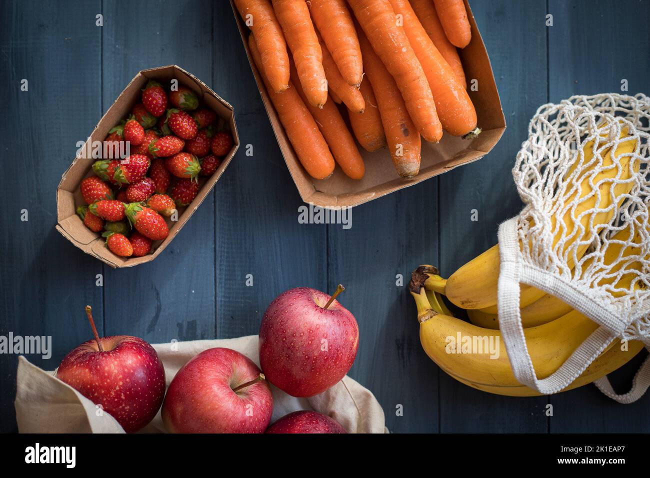 Verdure e frutta assortite in confezioni riutilizzabili di carta, legno e tessuto poste su un tavolo di legno blu. Concetto di imballaggio ecocompatibile. Vista dall'alto. Foto Stock
