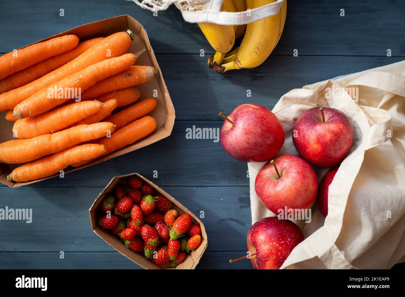 Verdure e frutta assortite in confezioni riutilizzabili di carta, legno e tessuto poste su un tavolo di legno blu. Concetto di imballaggio ecocompatibile. Vista dall'alto. Foto Stock