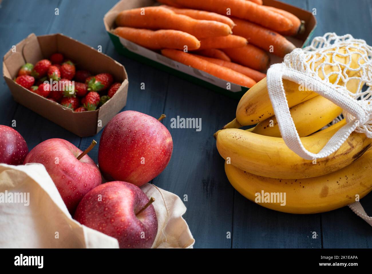 Verdure e frutta assortite in confezioni riutilizzabili di carta e tessuto poste su un tavolo di legno blu. Concetto di imballaggio ecocompatibile. Vista dall'alto. Foto Stock