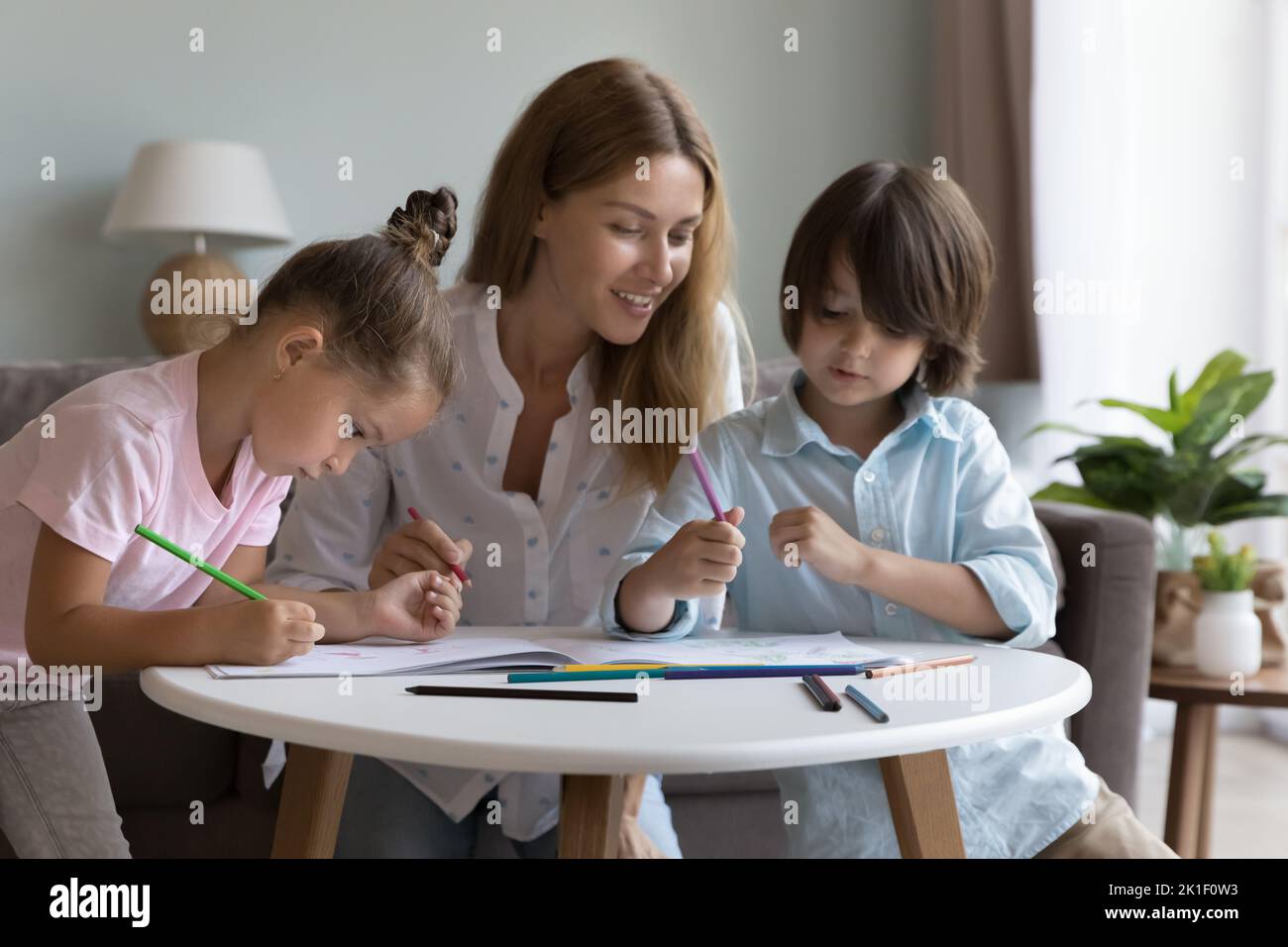 Madre felice che aiuta i bambini piccoli carini del fratello a disegnare Foto Stock