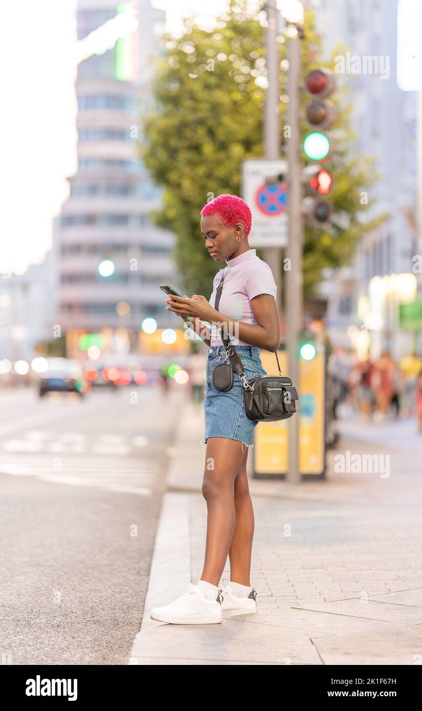 Giovane donna afro in piedi per strada utilizzando il cellulare Foto Stock