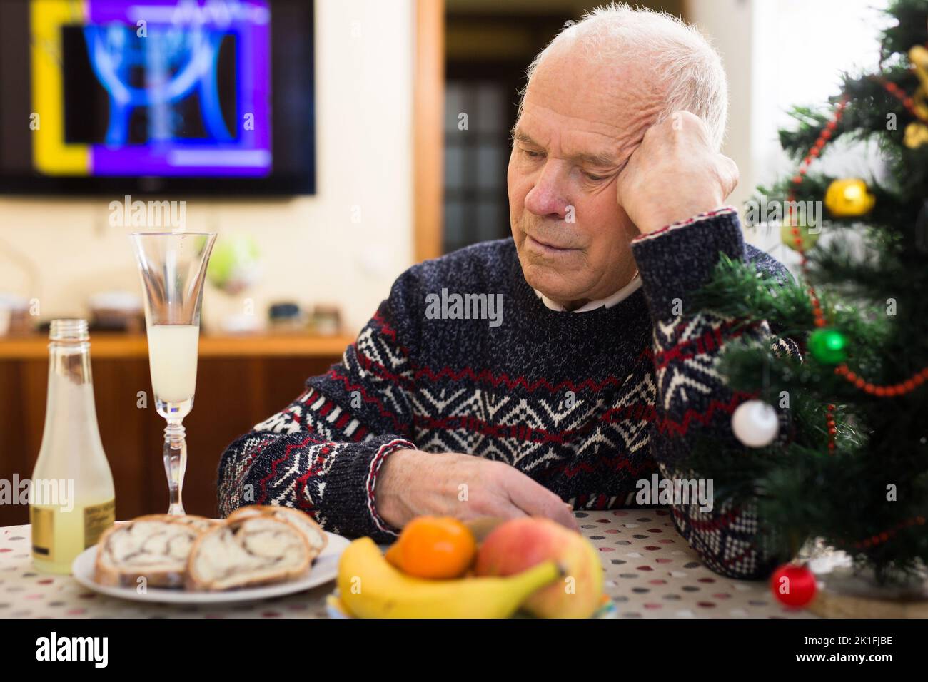 Solitario frustrato uomo anziano dai capelli grigi seduto al tavolo di casa durante la celebrazione di Natale Foto Stock