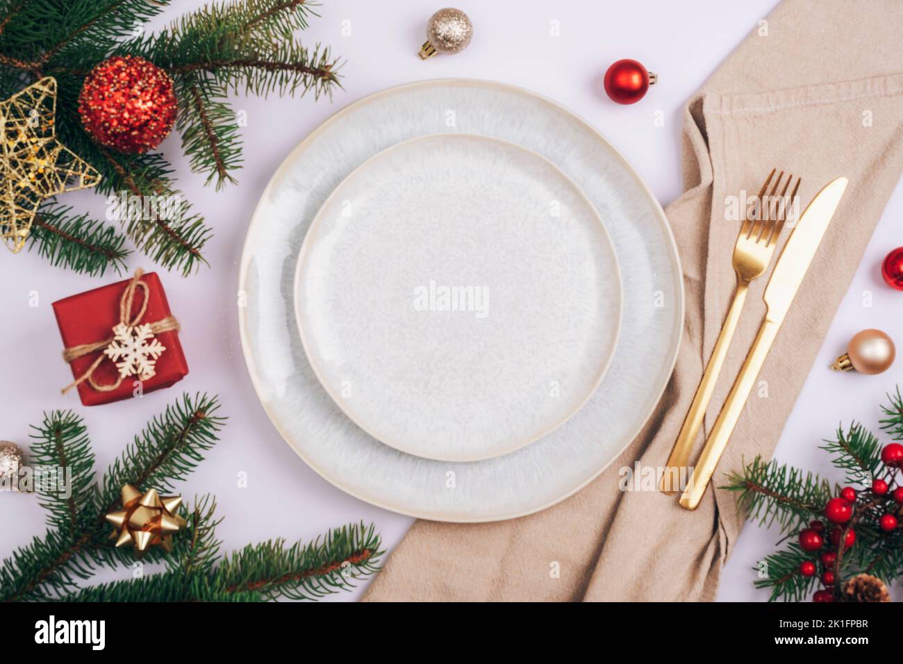 Tavolo elegante, rami di abete, stelle e palle con piatto bianco, posate e tovagliolo beige su tavolo bianco. Concetto di Natale. Vista dall'alto, disposizione piatta. Foto Stock