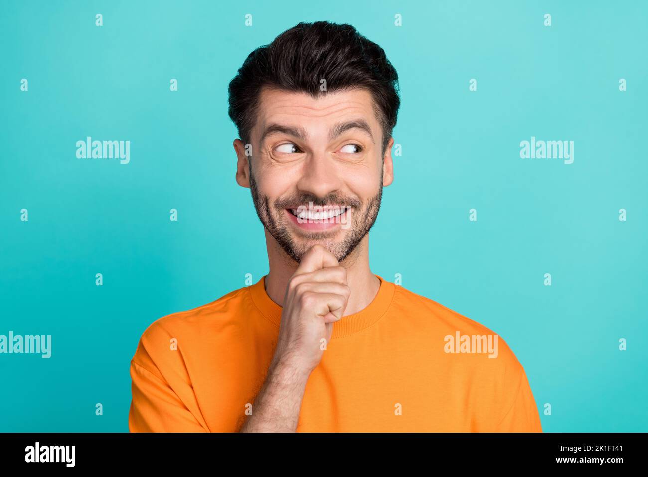 Primo piano foto di giovane bello attraente uomo indossare t-shirt arancione tocco mento barba sorriso positivo sguardo occupato spazio vuoto affare isolato su aquamarine Foto Stock