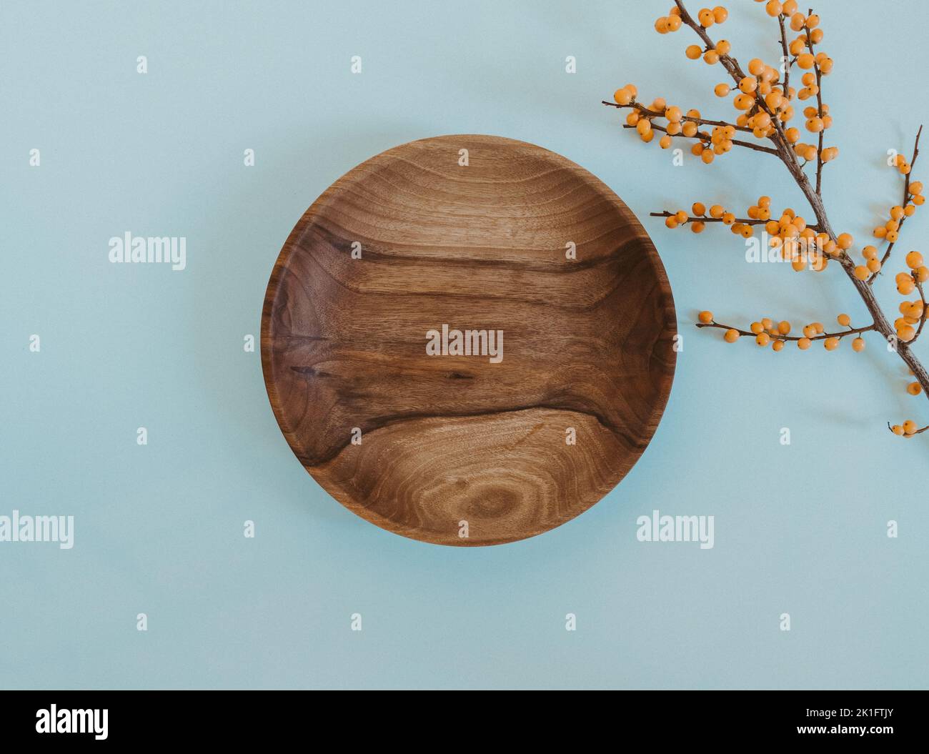 Mockup piatto di legno rotondo per eco, cibo o prodotti di bellezza e ramificazione con bacche d'arancia su sfondo blu. Vista dall'alto. Spazio di copia Foto Stock