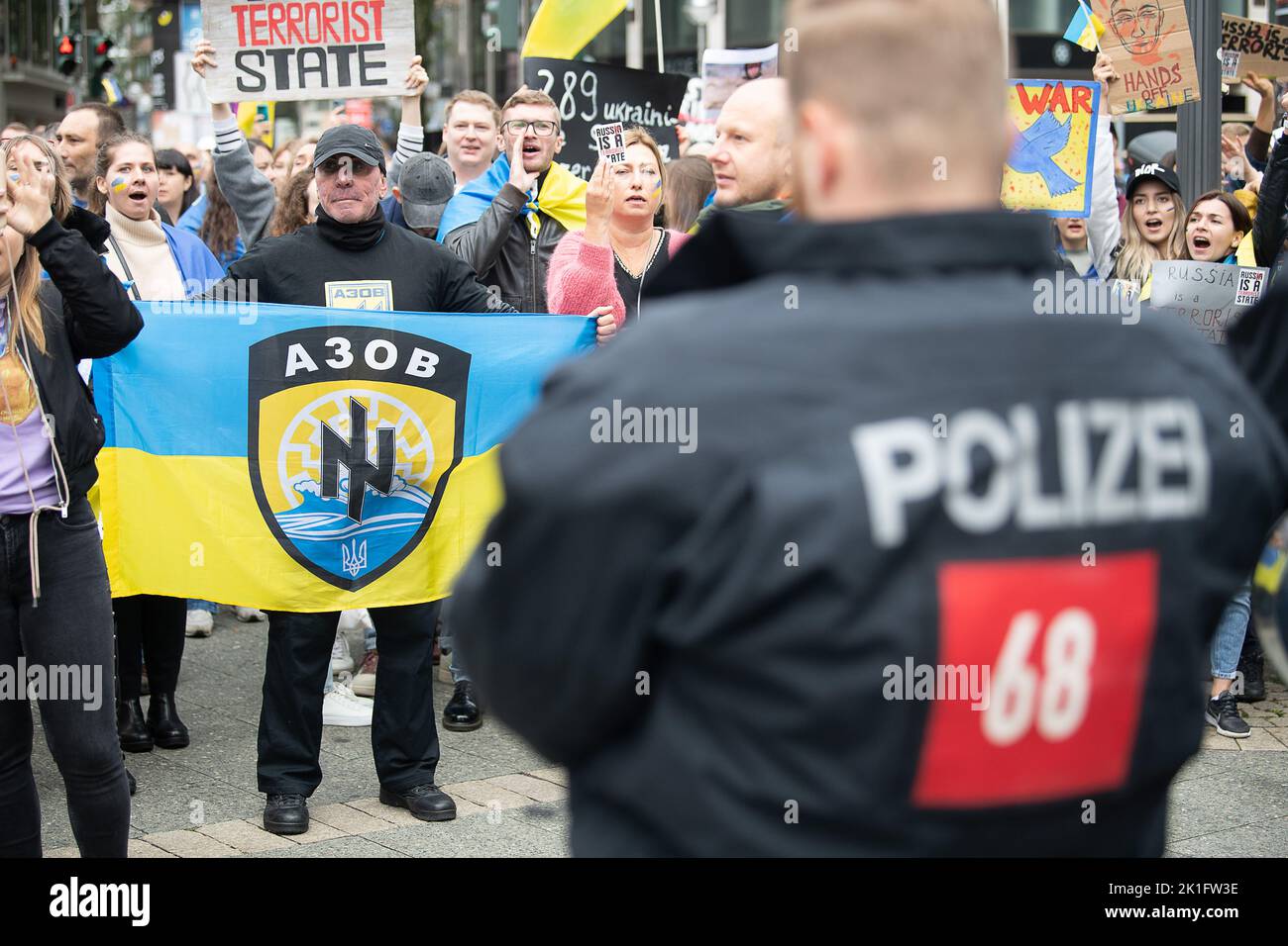 18 settembre 2022, Hessen, Francoforte sul meno: Un dimostratore pro-ucraino tiene una bandiera nei colori dell'Ucraina con lo stemma del battaglione Azov, nella versione fino al 2015, durante una contro-dimostrazione ad una dimostrazione pro-russa in Piazza dell'Opera. Sullo stemma si trova un cosiddetto "sole nero" stampato in bianco e una linguetta di lupo. Entrambi i simboli, che erano e sono utilizzati anche da estremisti di destra e nazionalisti. Domenica, nella metropoli principale, manifestanti pro-russi protestano contro le sanzioni contro la Russia. Allo stesso tempo, una contro-dimostrazione in sup Foto Stock