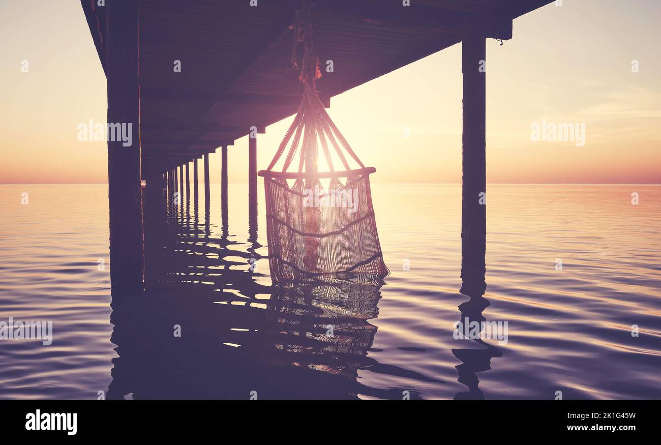 Silhouette di un'amaca in acqua sotto un molo al tramonto, tonalità di colore applicato. Foto Stock