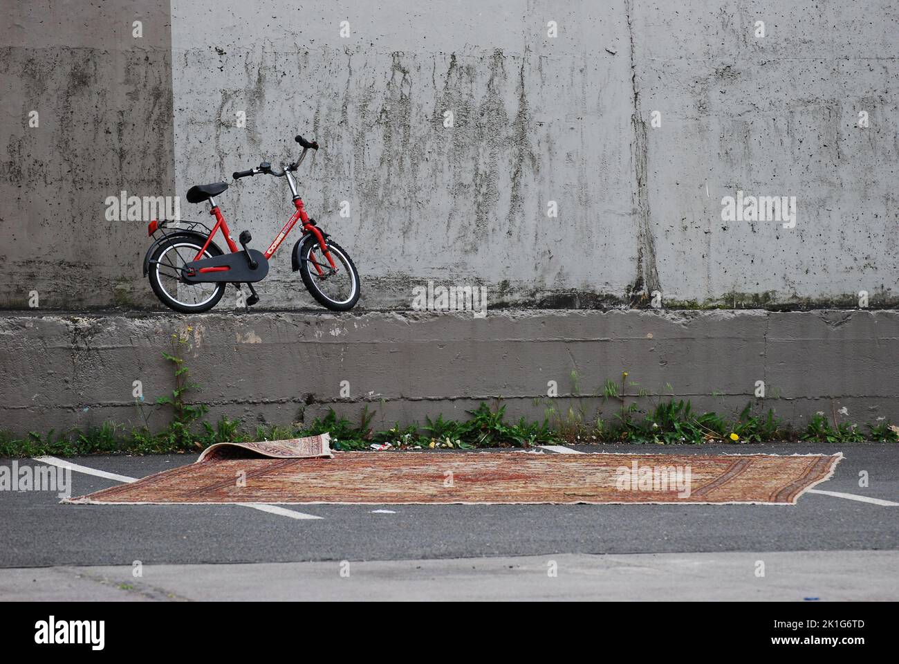 Una bici rossa per bambini davanti a una parete di cemento e un tappeto orientale a Essen, NRW, Germania Foto Stock