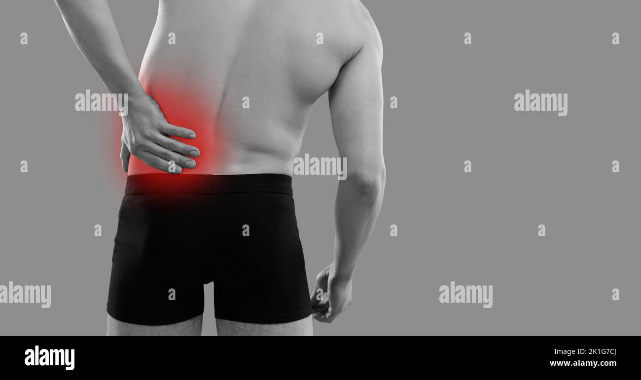 L'uomo che soffre di mal di schiena o di dolore nel suo lato sinistro in piedi su sfondo grigio Foto Stock