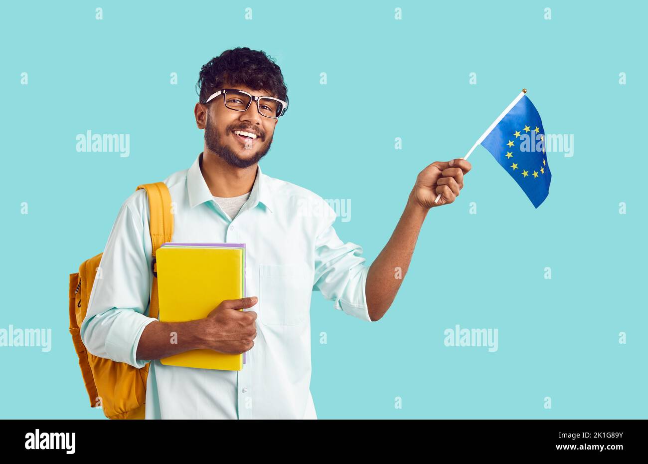 Un'università studentesca indiana positiva con zaino e libri di testo che sventolano la bandiera dell'Unione europea Foto Stock