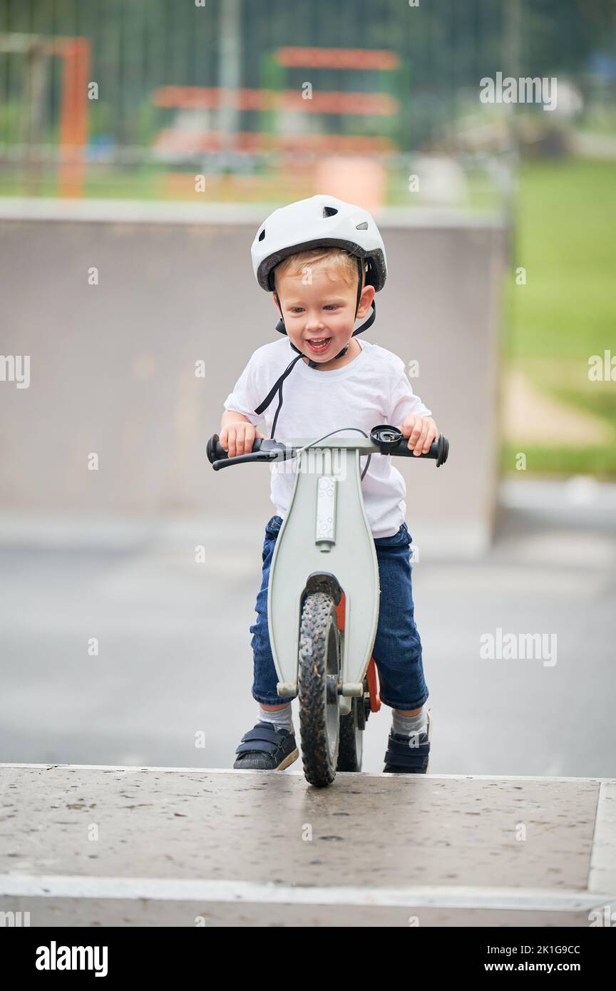 Happy bambino equitazione Balance bike. Bambino maschio in casco imparando a correre in bicicletta al parco skate. Foto Stock