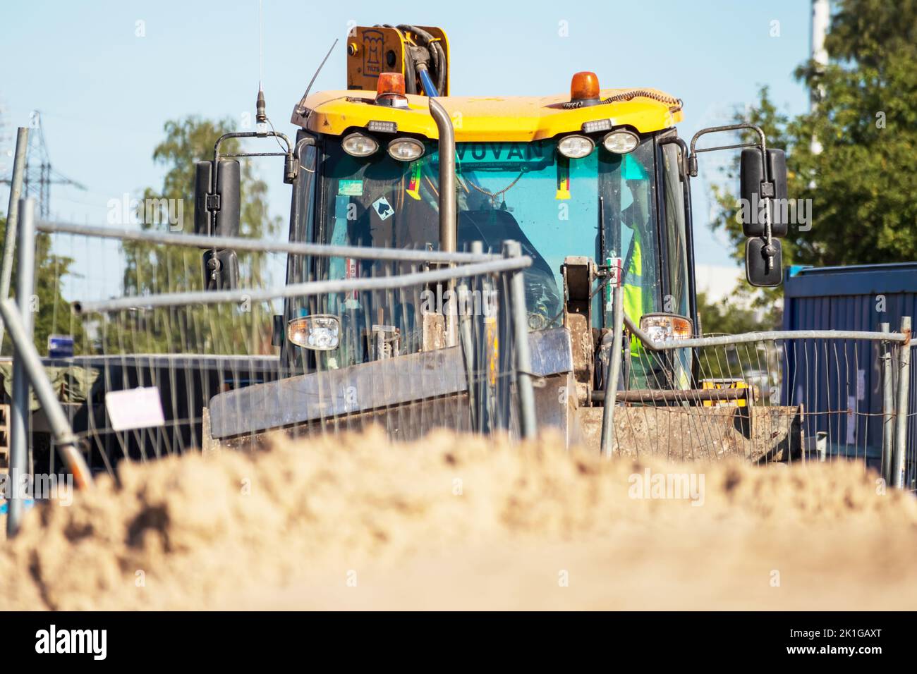 Gru gialla su un cantiere di ghiaia con cielo blu e alberi verdi sullo sfondo Foto Stock