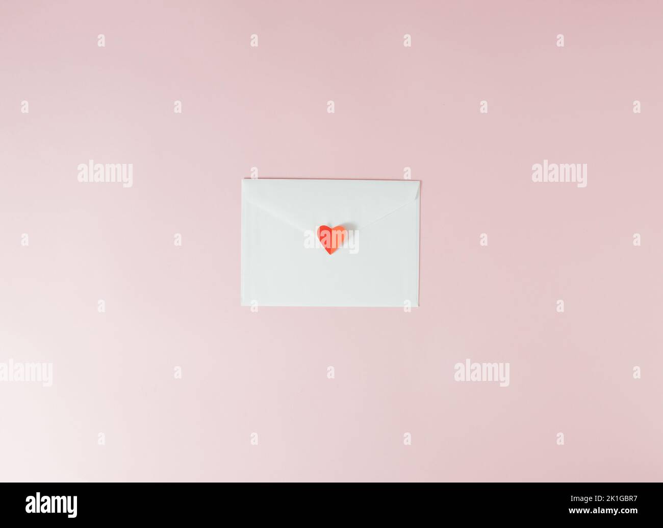 Lettera d'amore per San Valentino in busta bianca su sfondo rosa pallido e con cuore rosso. Concetto minimo. Foto Stock