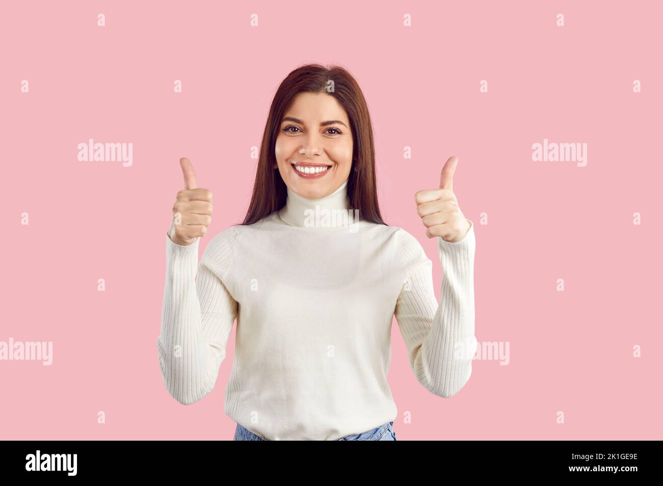 Felice bella giovane donna isolata su sfondo rosa mostrando pollici su e sorridendo Foto Stock