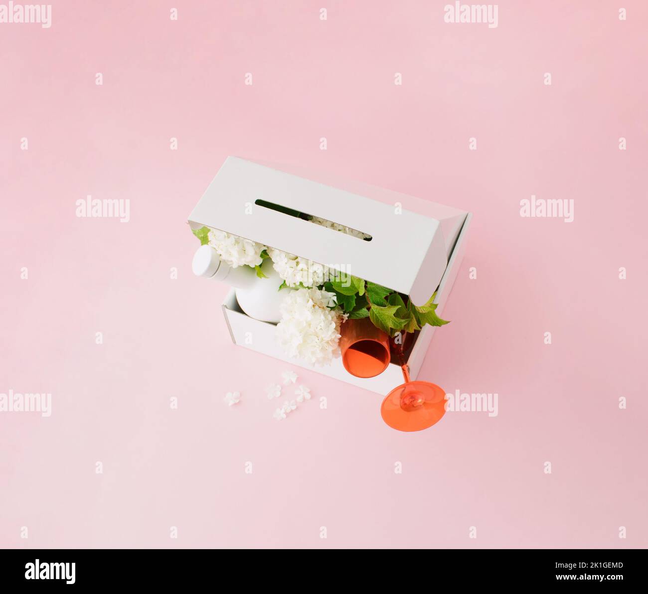 Scatola regalo bianca con fiori bianchi, due bicchieri rossi e bottiglia bianca su sfondo rosa. Foto Stock