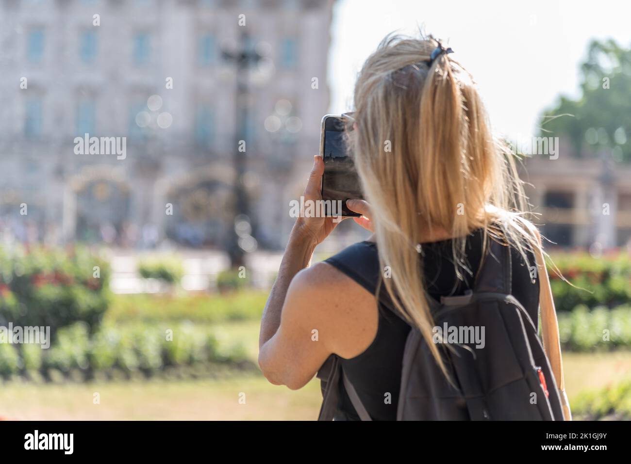 Vista posteriore di una donna bionda che scatta una foto da smartphone di Buckingham Palace fuori fuoco. Foto Stock