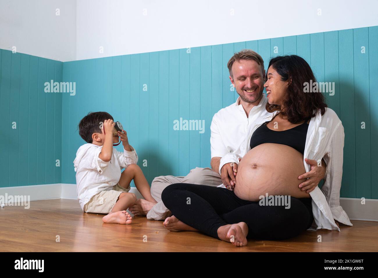 Foto di giovane giovane allegra coppia sorridente, moglie incinta e marito con il figlio a casa Foto Stock