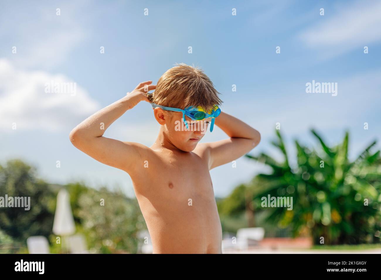 il ragazzo di 8 anni si mette gli occhiali da nuoto e si prepara a nuotare nella piscina dell'hotel. Foto Stock