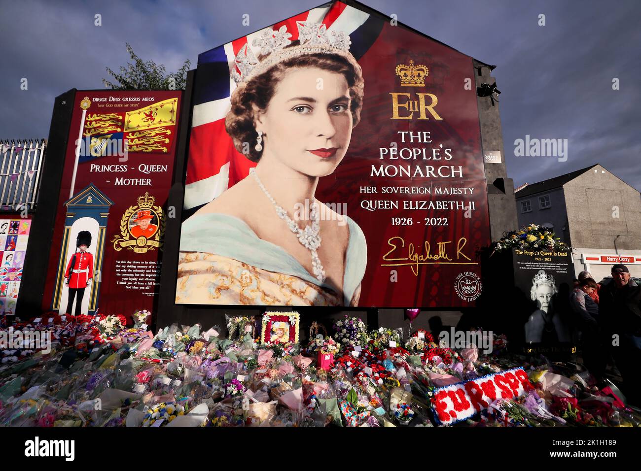 Dopo la scomparsa del Monarca britannico, la gente depone fiori in un murale raffigurante la Regina Elisabetta II sulla Shankill Road a Belfast. Foto Stock