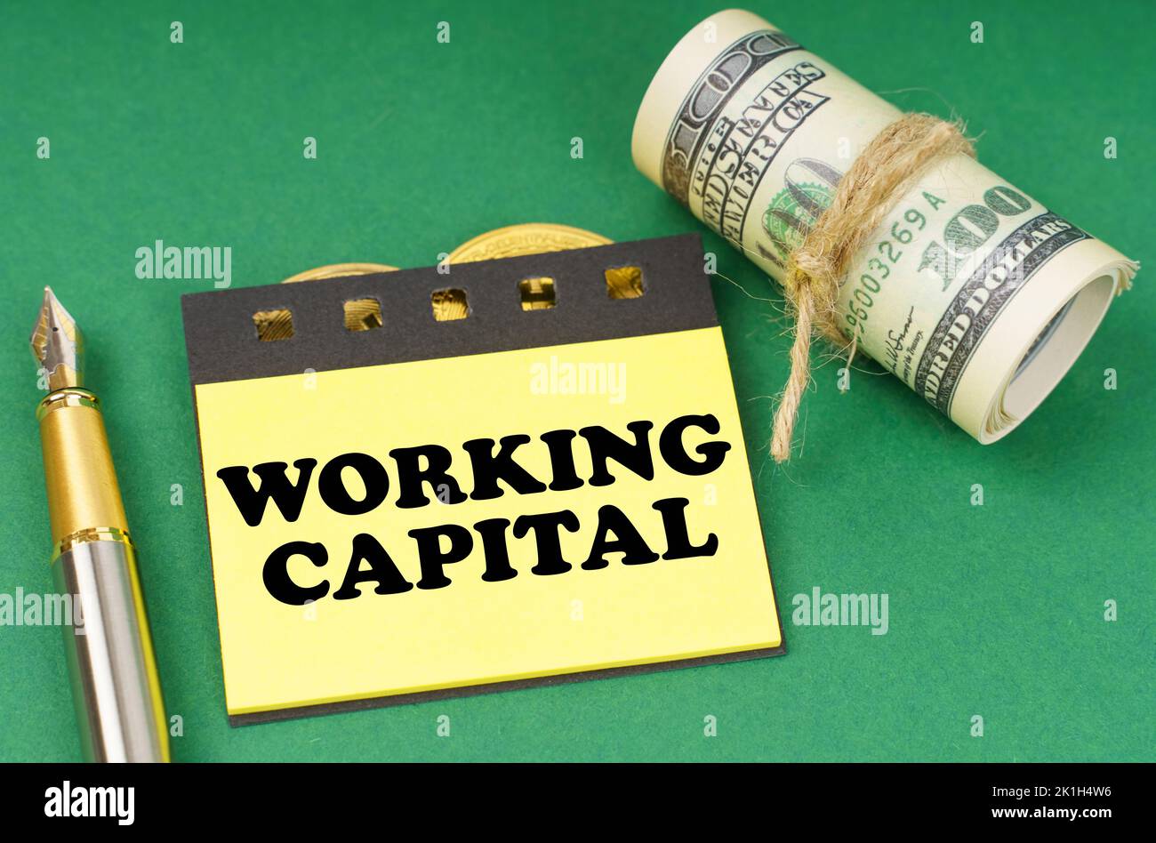 Concetto aziendale. Su una superficie verde ci sono una penna, dollari e adesivi gialli con l'iscrizione - Working Capital Foto Stock
