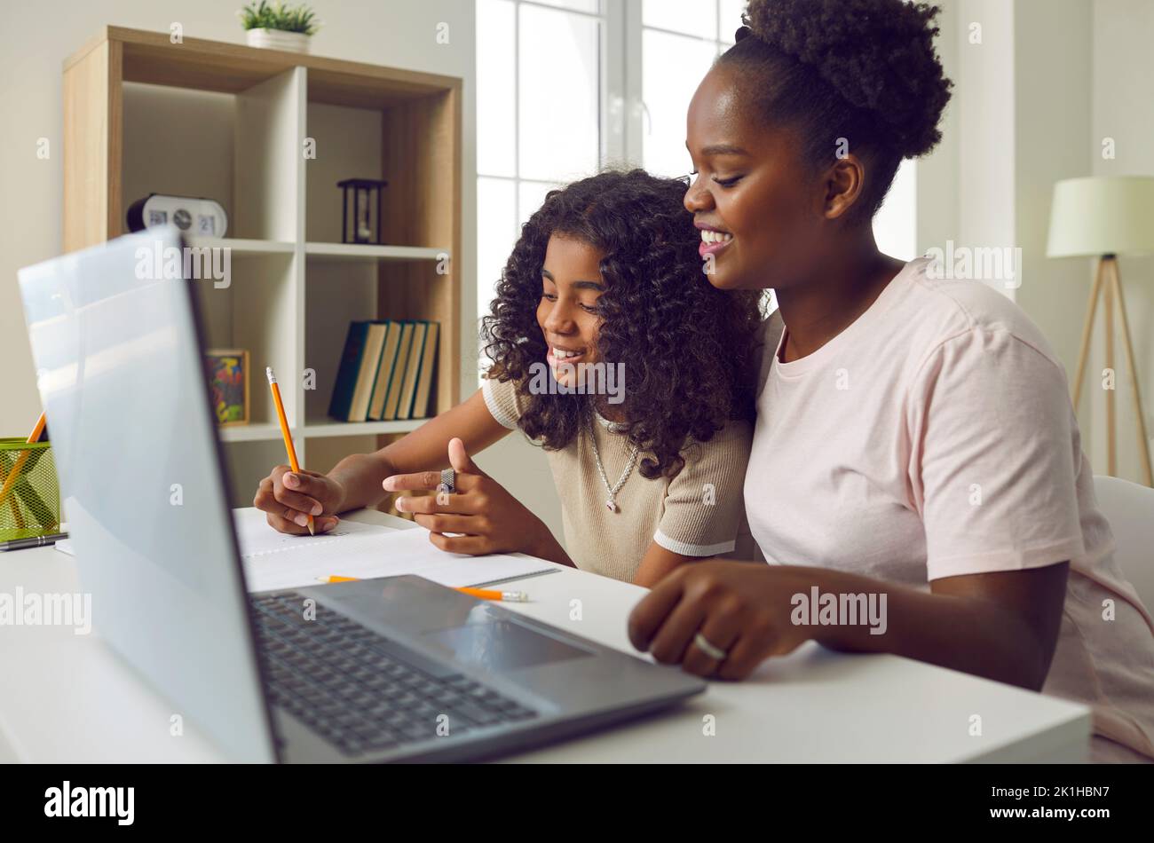 Felice giovane madre afro-americana che aiuta la figlia piccola con i compiti a casa della scuola Foto Stock